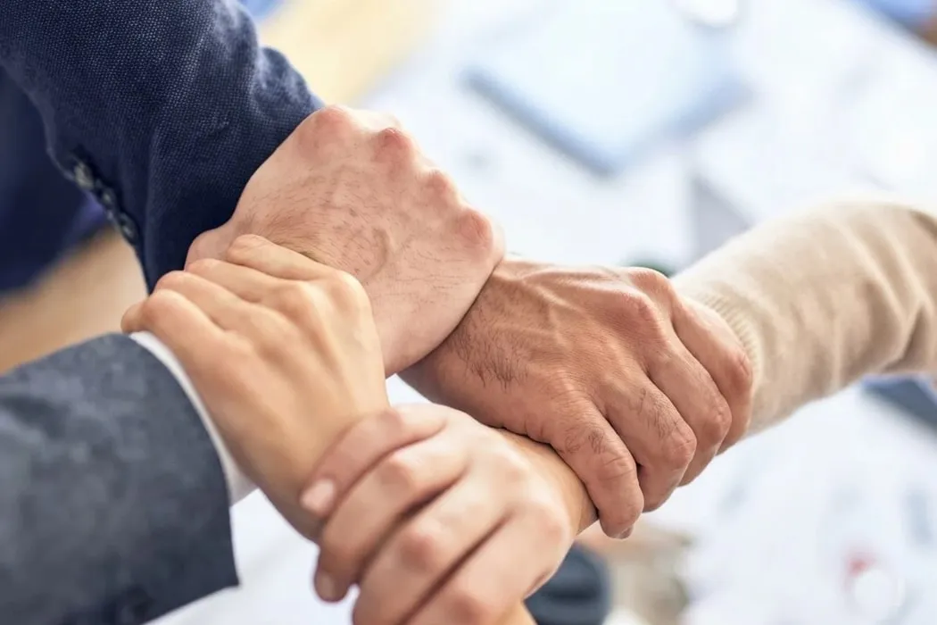 Four hands clasped together at the wrists, a sign of partnership